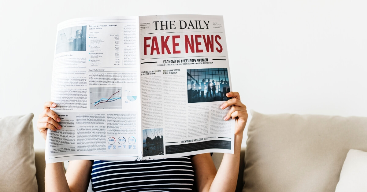 woman holding newspaper in front of face with headline fake news