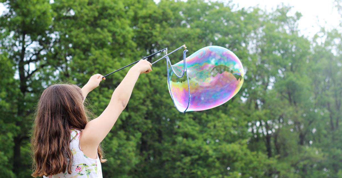 Young Girl playing using string and pole to create huge blown bubble