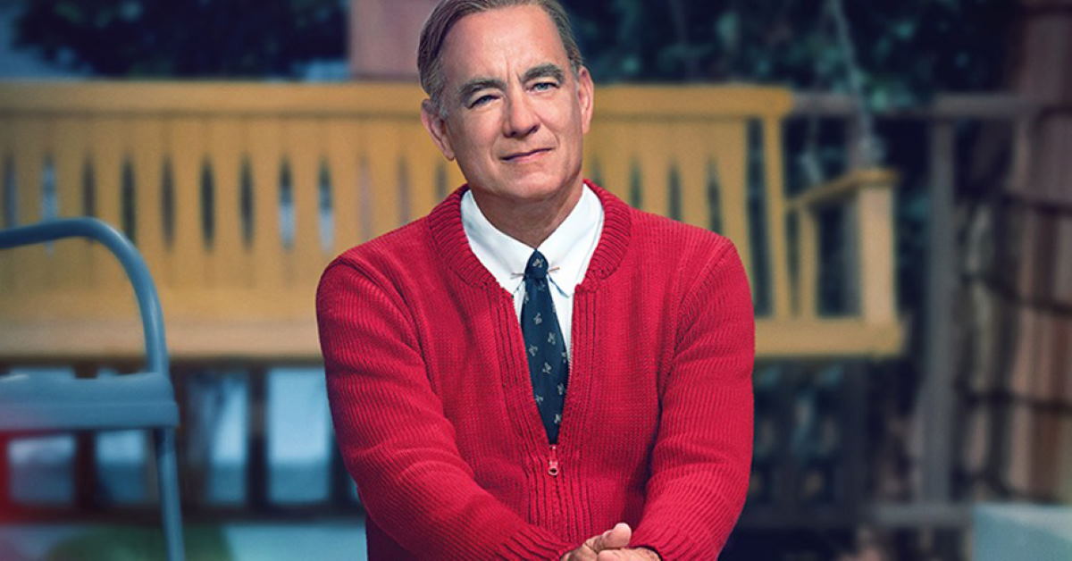 tom hanks portraying Mr Rodgers sitting on a step in a shirt and tie with a bright red cardigan