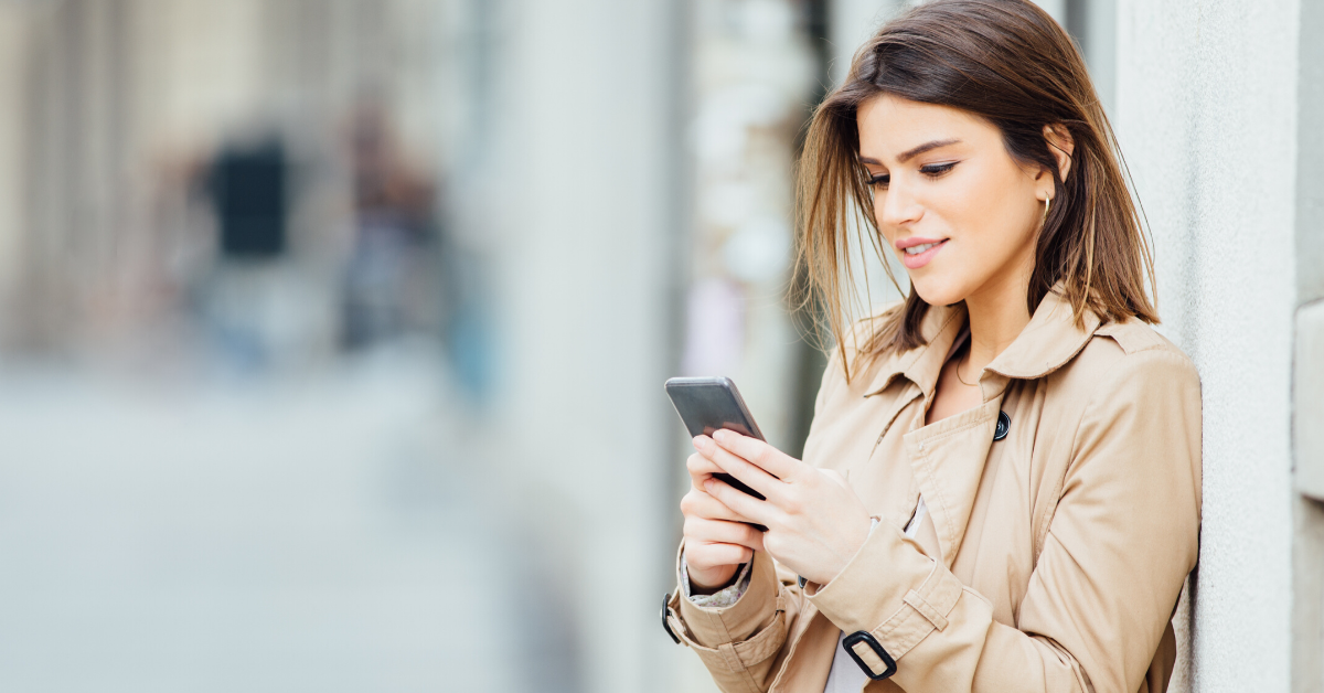 woman leaning against wall smiling looking down at mobile phone