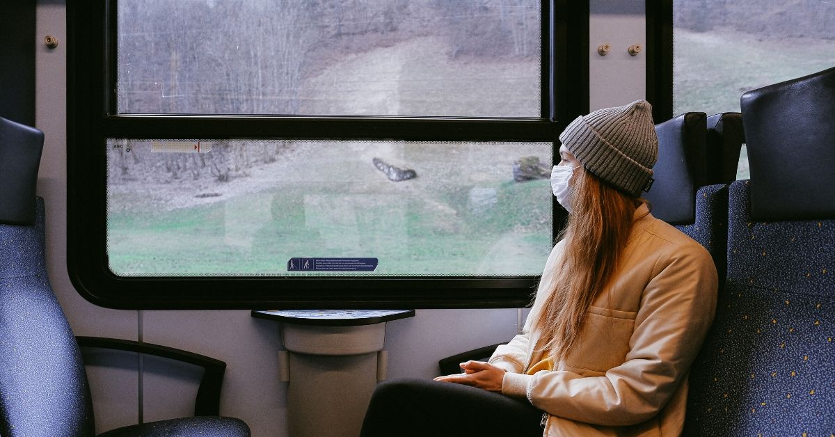 photo of a woman sitting on a train gazing out the window wearing a mask