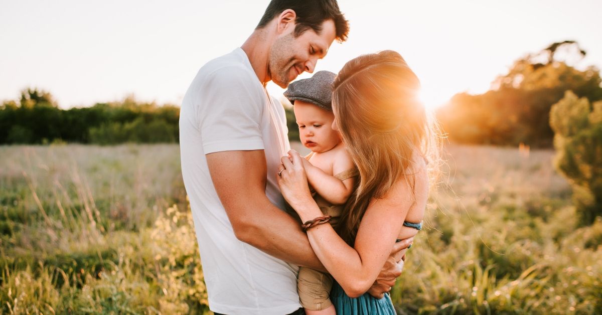 photo of a young family and baby standing in a field backlit by the sun