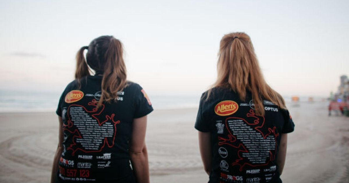 photo of the backs of two girls wearing red frogs shirts on the beach
