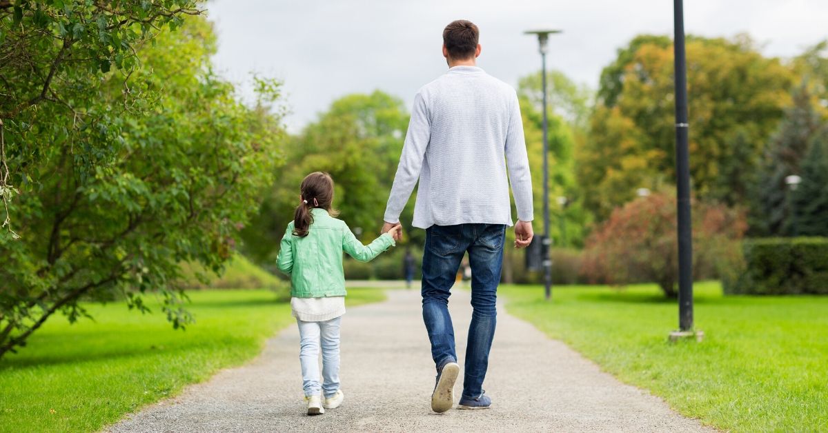 photo of a girl and dad holding hands walking in a park