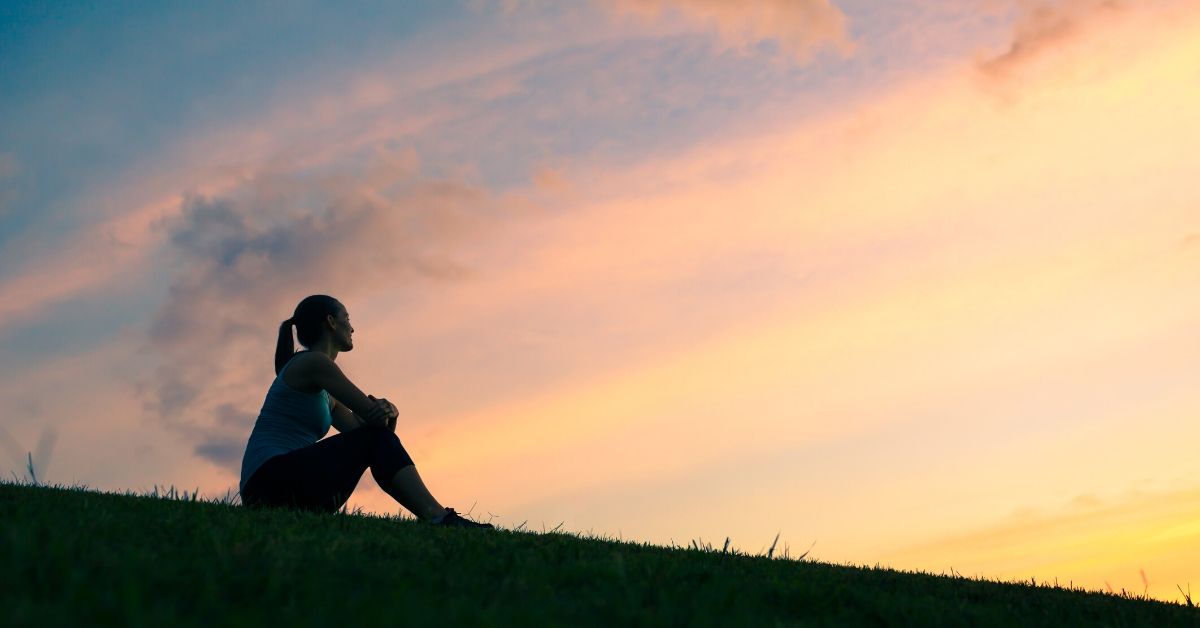 photo of a woman's profile silhouette as she sits on a hill with a sunset behind her