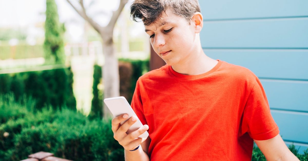 photo of a boy wearing a red shirt on his phone outside in the yard