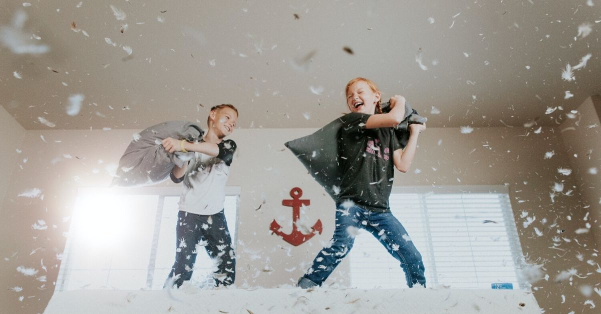 photo shows two kids having a pillow fight has feathers rain down around them