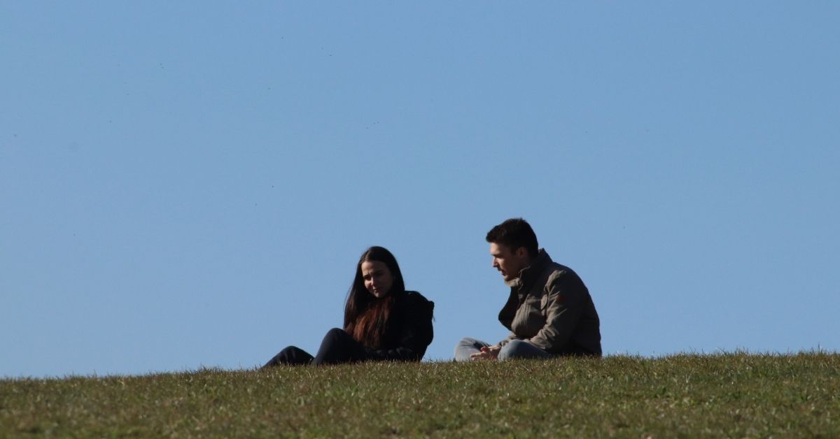 woman and man sitting on a hill together talking