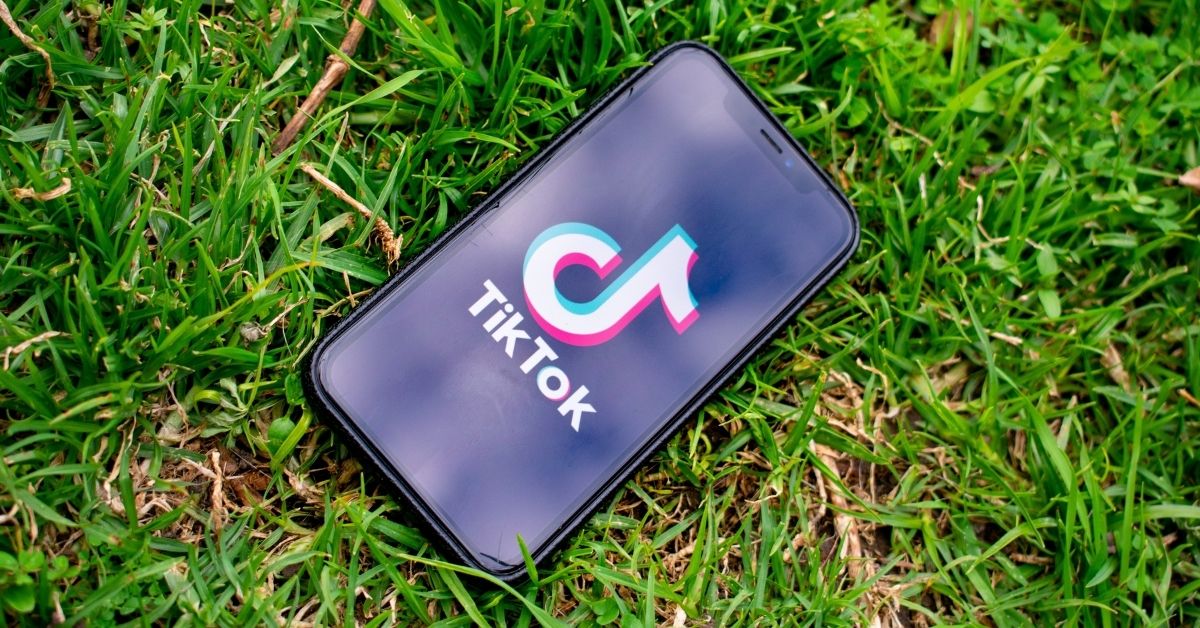 a phone displaying the tik tok app lies on the grass