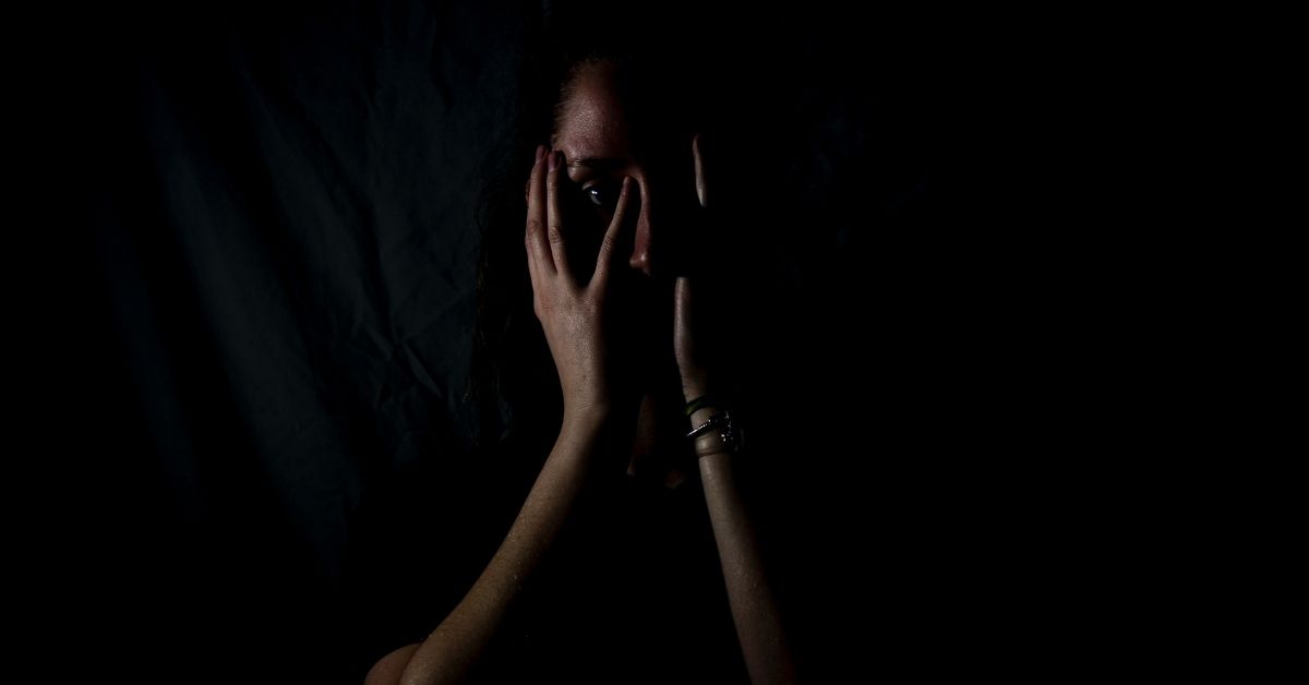 girl hiding face behind hands in dark room