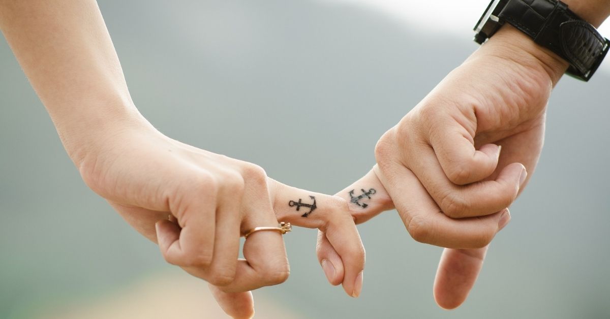 matching anchor tattoo on a couple's interlocked fingers