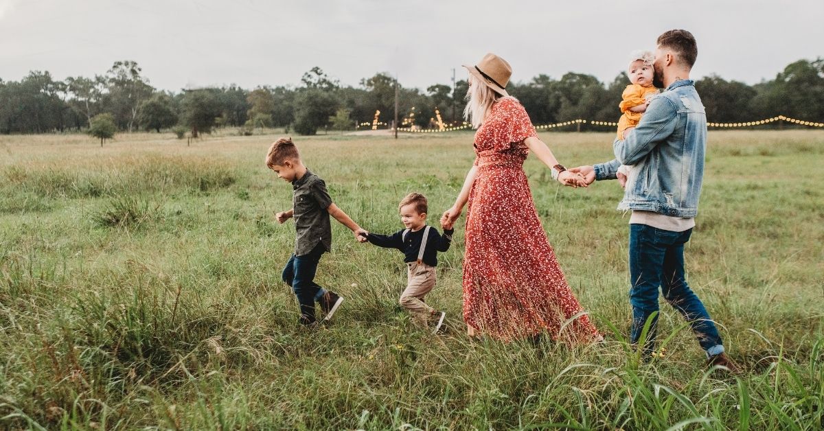 perfect model family holding hands walking through a field