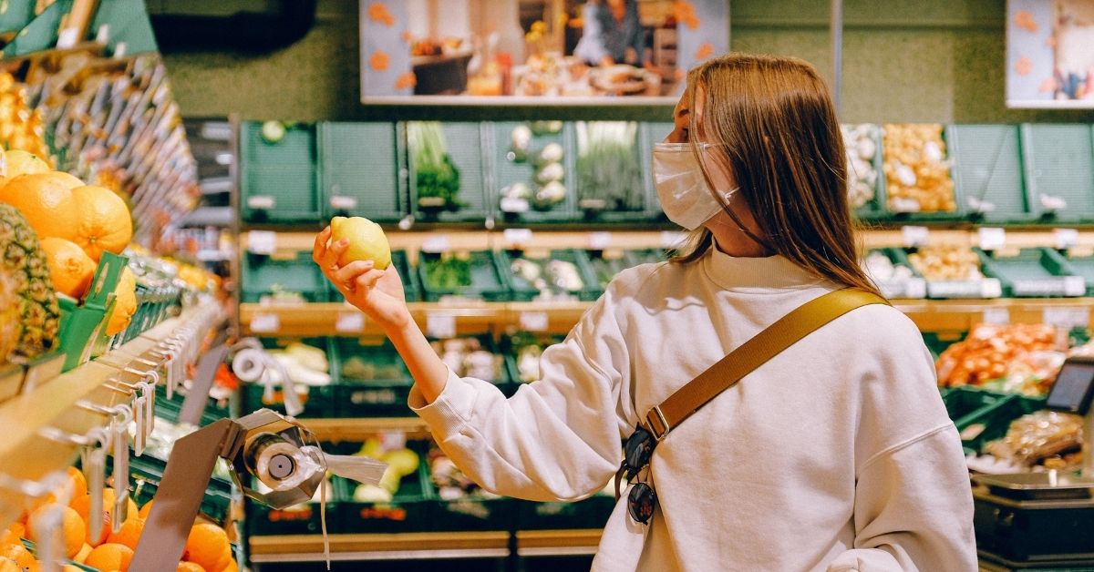 woman wearing a mask picking up an orange in the supermarket
