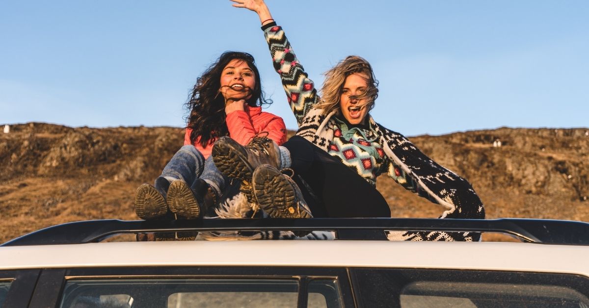 two girls on a roadtrip sitting on top of a car