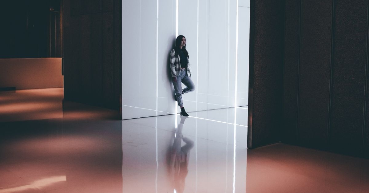 a girl leans against a wall, alone in a big room