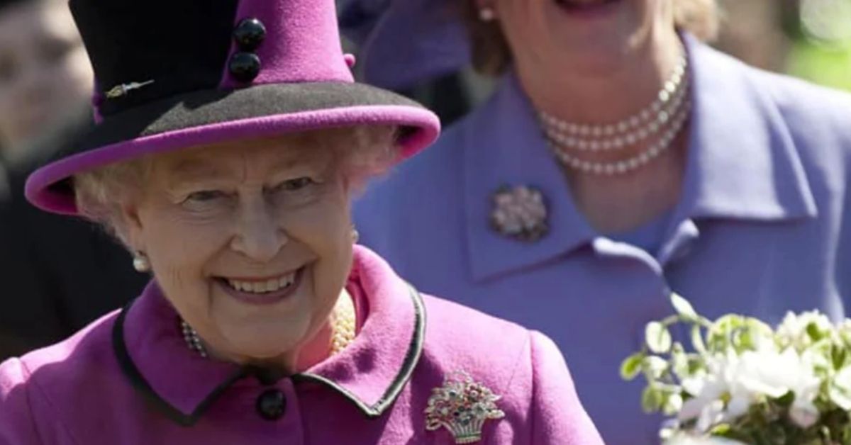 the queen in her purple outfit smiling as she walks ahead