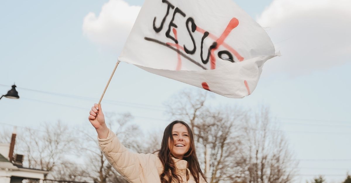 a woman waves a handmade flag which says jesus