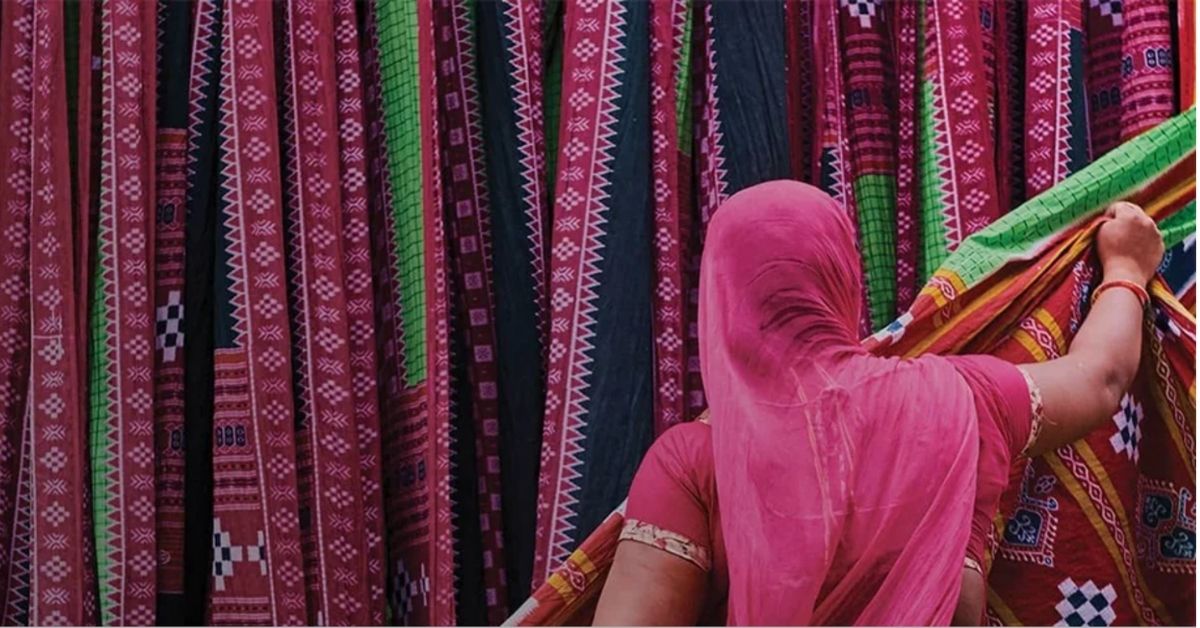 a woman wearinga bright pink burka is surrounded by beautiful coloured fabrics