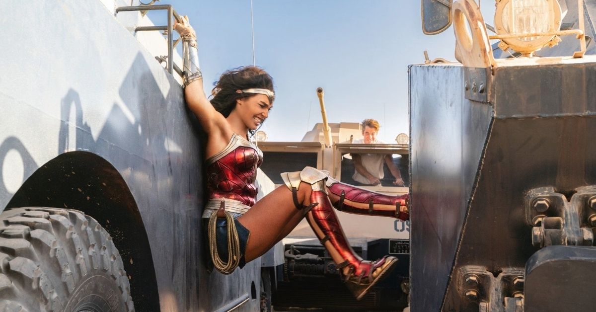 an action shot of wonder woman wedged between two moving trucks pushing with her legs