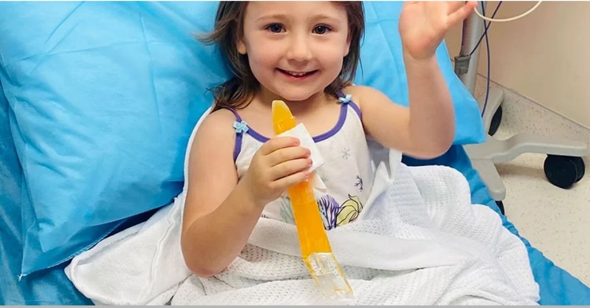 cleo smith eating an icy pole smiling and waving from hospital bed